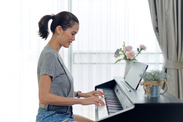 Azjatycka piękna kobieta bawić się elektronicznego pianino w domu.