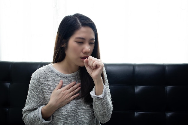 Azjatycka piękna kobieta siedzi w salonie kaszle i dotyka dłonią jej klatki piersiowej Koncepcja opieki zdrowotnej