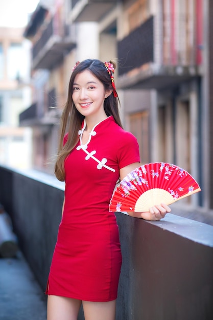 Azjatycka piękna kobieta w czerwonej sukience stoi trzymając wentylator wśród starego centrum chińskiego nowego roku tematu