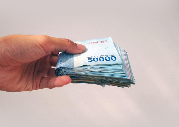 Azjatycka ręka daje trochę pieniędzy w indonezyjskiej walucie na białym tle