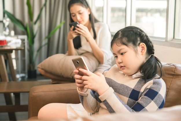 Azjatycka rodzina mama i córka spędzają weekend razem z ręcznym korzystaniem ze smartfona w koncepcji pomysłów na technologię domu w salonie