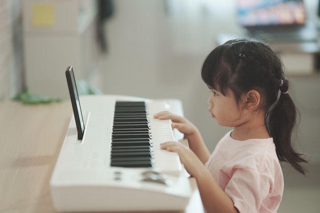 Azjatycka śliczna dziewczyna ucząca się online muzyki fortepianowej z nauczycielem przez telefon komórkowy lub tablet Pomysł zajęć dla dziecka w domu podczas kwarantanny Koncepcja uczenia się muzyki online