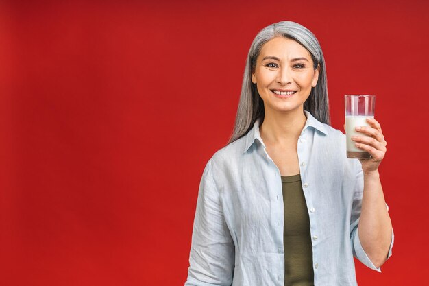 Azjatycka starsza dojrzała kobieta w wieku do picia mleka do żywności wapniowej i koncepcji zdrowego stylu życia na białym tle na czerwonym tle