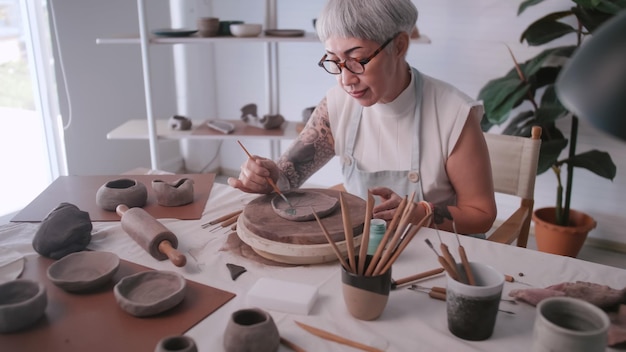 Zdjęcie azjatycka starsza kobieta korzystająca z pracy garncarskiej w domu ceramika tworzy nową ceramikę w studiu