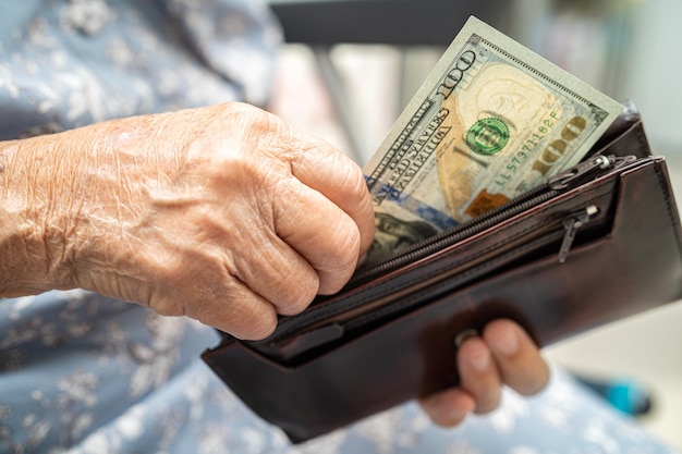 Azjatycka starsza kobieta trzymająca i licząca banknoty dolara amerykańskiego w torebce Problem oszczędzania ubóstwa na emeryturze