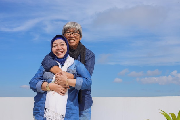 Azjatycka starsza para w swobodnym stylu uśmiecha się staruszek przytula swoją żonę na tle błękitnego nieba