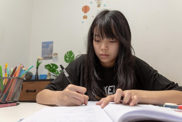 Azjatycka studentka pisze pracę domową i czyta książkę przy biurku