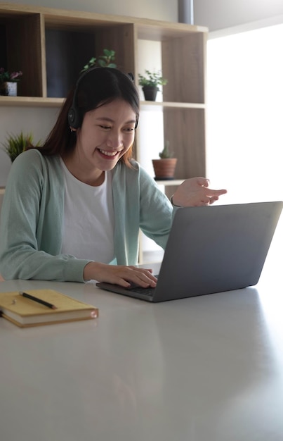 Azjatycka studentka w zwykłych ubraniach wyjaśniająca pracę domową na wideokonferencji z nauczycielami na laptopach w domuxA