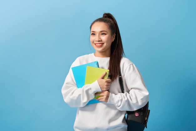 Azjatycka studentka z plecakiem trzymająca zeszyty na jasnoniebieskim tle