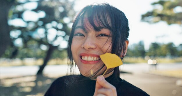 Azjatycka szczęśliwa kobieta w parku i liście z twarzą i odkrywać naturę dla dobrego samopoczucia i środowiska na świeżym powietrzu rośliny słoneczne i portret podróż i przygoda w ogrodzie publicznym z uśmiechem w podróży
