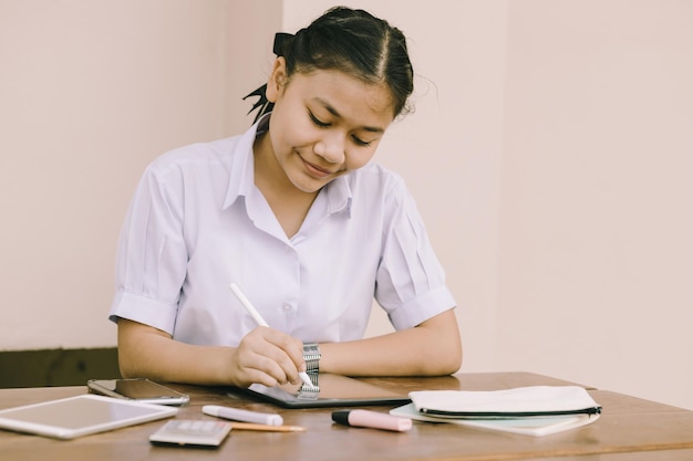 Azjatycka tajska ładna dziewczyna nastolatek uczeń mundurek szkolny szczęśliwy uśmiech za pomocą komputera typu Tablet do pracy domowej i e-learningu samodzielna edukacja szczęśliwa koncepcja uśmiechu