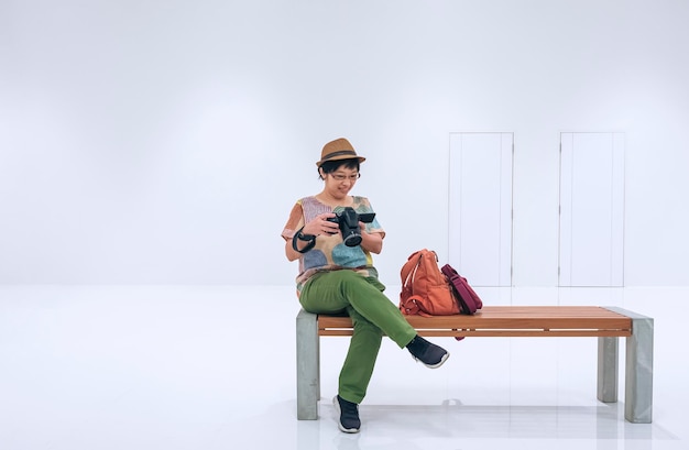 Azjatycka turystka sprawdza zdjęcie w aparacie cyfrowym, siedząc na ławce w białym przejściu