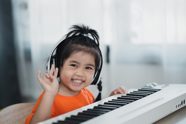 Azjatycka Urocza Dziewczyna W Słuchawkach Ucząca Się Muzyki Fortepianowej Online Z Nauczycielem Przez Telefon Komórkowy Lub Tablet Pomysł Zajęć Dla Dziecka W Domu Podczas Kwarantanny Koncepcja Nauki Muzyki