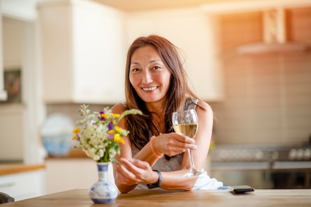 Azjatycka uśmiechnięta kobieta rozmawiająca z przyjaciółmi przy lampce wina w domu