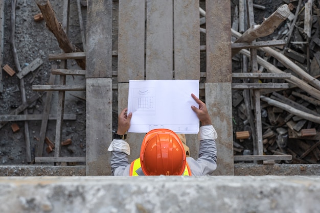 Azjatycki architekta mienia projekta projekt tapetuje i jest ubranym hełm przy budową