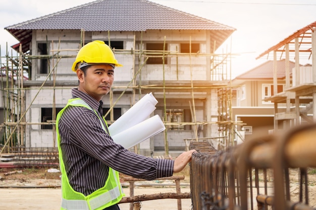 Azjatycki biznes człowiek inżynier budowlany pracownik w kasku ochronnym i papier plany pod ręką, patrząc na stalowy pręt na placu budowy domu