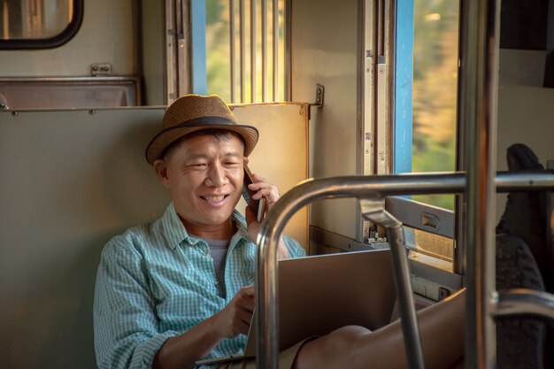 Azjatycki biznesmen pracujący online z laptopem i telefonem komórkowym czuje się zrelaksowany podczas podróży pociągiem