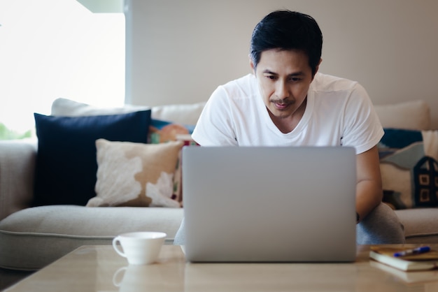 Azjatycki biznesmen siedzi w domu na kanapie i pracuje na laptopie