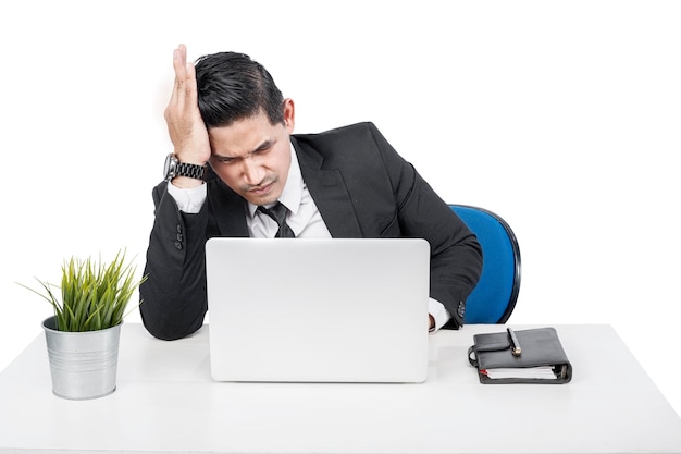 Azjatycki biznesmen siedzi z laptopem na biurku z zaakcentowanym wyrazem twarzy