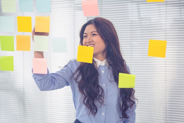 Azjatycki bizneswoman używa kleiste notatki na ścianie w biurze