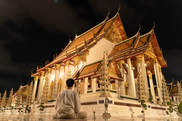Azjatycki buddyjski mężczyzna ubrany w tradycyjny strój z Tajlandii, siedzący do medytacji, aby oddać szacunek posągowi Buddy w Wat Suthat Thepwararam w buddyjski święty dzień Buddyjski dzień sabatu