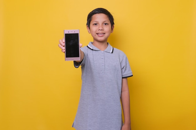 Azjatycki chłopak w swobodnym stylu uśmiecha się i pokazuje ekran smartfona na żółtym tle