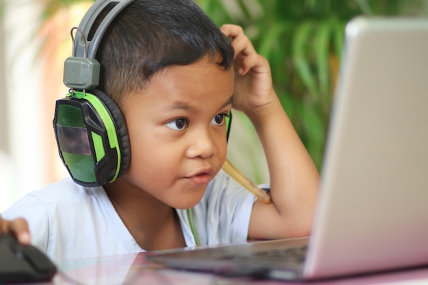 Azjatycki chłopiec dziecko siedzi przy stole z laptopem i przygotowuje się do szkoły. Koncepcja edukacji online. Nauka lekcji online podczas wideokonferencji.