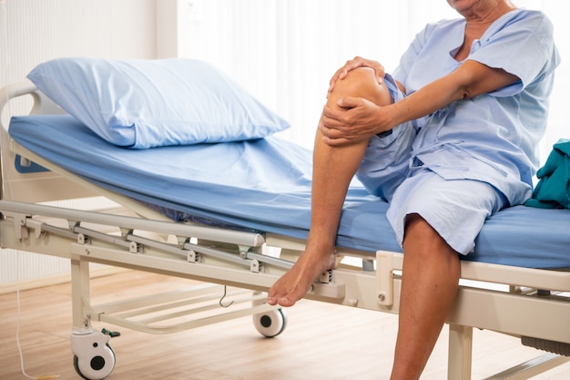 Azjatycki cierpliwy mężczyzna czuje ból na jego kolanie przy sala szpitalną.