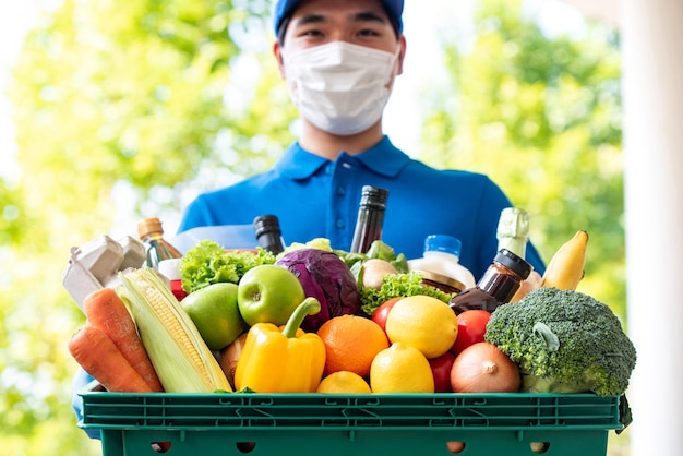 Azjatycki Doręczyciel Noszący Maskę Na Twarz Trzymający Kosz Spożywczy Na Zewnątrz, Higieniczna Usługa Dostarczania żywności W Czasie Koncepcji Pandemii