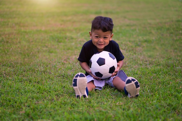 Azjatycki dzieciak bawić się piłkę nożną lub futbol w parku
