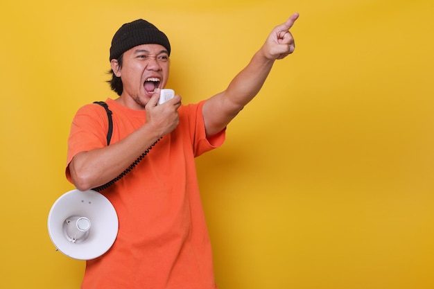 Azjatycki facet na co dzień na żółtym tle krzyczy przez megafon i wskazuje palcem w górę