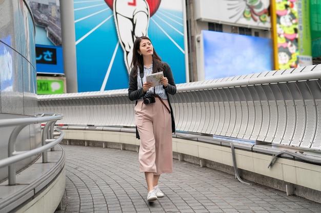 azjatycki gość spacerujący po moście w Dontonbori. trzymając mapę i szukając miejsc docelowych.