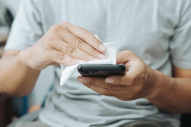 Azjatycki Indonezyjczyk wyciera i oczyszcza smartfon za pomocą papieru tkaninowego na rękach