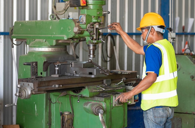 Azjatycki inżynier robotnik w fabryce maszyn wiertniczych w inteligentnej fabryce w żółtym hełmie ochronnym przed małą fabryką