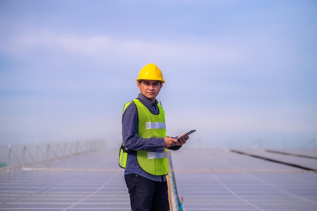 Azjatycki inżynier stojący na dachu fabryki i sprawdzający energię słoneczną energii ogniw słonecznych za pomocą technologii tabletu