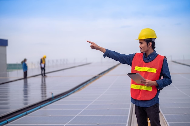 Azjatycki inżynier stojący na dachu fabryki i sprawdzający energię słoneczną energii ogniw słonecznych za pomocą technologii tabletu