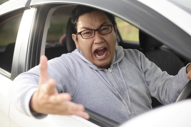 Azjatycki kierowca wścieka się i wścieknie z powodu ruchu drogowego krzycząc i wskazując z samochodu