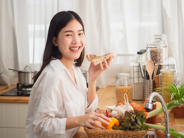 Azjatycki kobiety łasowania chleb podczas gdy przygotowywający jedzenie w kuchni