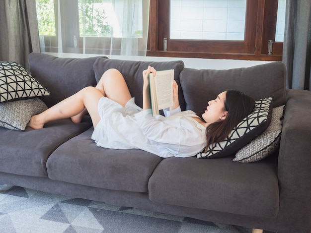 Azjatycki kobiety obsiadanie i czytająca książka na kanapie w domu