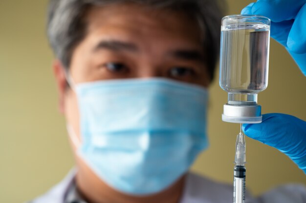 Azjatycki lekarz-mężczyzna nosi rękawicę medyczną i maskę na twarz, trzymając strzykawkę, która przyjmuje szczepionkę przeciwko koronawirusowi Covid 19, aby badać i analizować próbki przeciwciał dla pacjenta. Pojęcie chorób, opieka medyczna