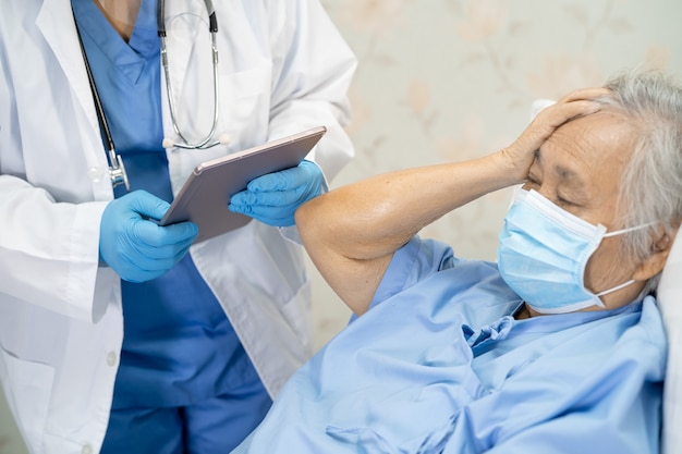 Azjatycki lekarz noszący osłonę twarzy i środki ochrony osobistej pasuje do nowego standardu, aby sprawdzić, czy pacjent chroni infekcję bezpieczeństwa Covid 19 Wybuch epidemii koronawirusa na oddziale pielęgniarskim kwarantanny.