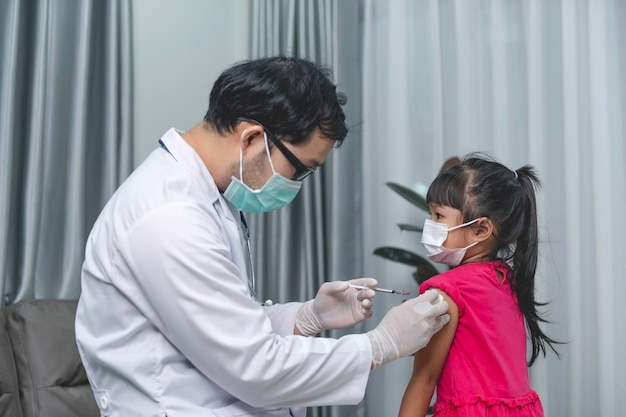 Azjatycki lekarz szczepionka do wstrzykiwań chroniąca przed wirusem covid19 dziewczynce noszą maskę medyczną. Ludzie to dziewczynki co roku szczepione przeciwko grypie