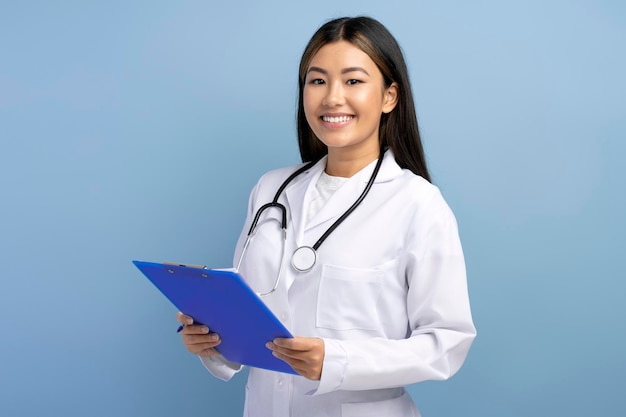 Zdjęcie azjatycki lekarz w białej sukni medycznej ze stetoskopem na ramionach, robiący notatki