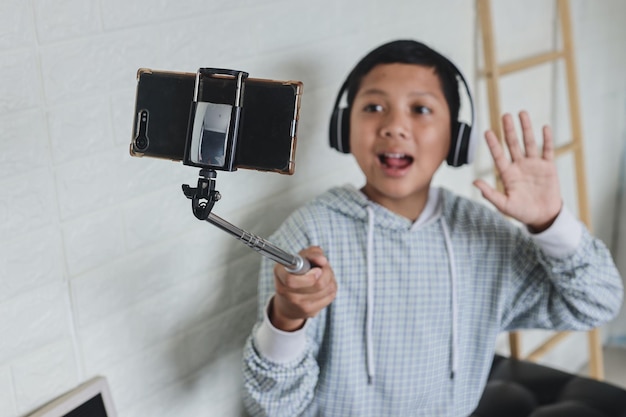Azjatycki mały wpływowy chłopiec nagrywa wideo ze smartfona, komunikuje się z subskrybentami, bierze se