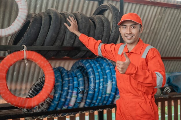 Azjatycki mechanik mężczyzna w worku z kciukami do góry stoi z regałem do opon