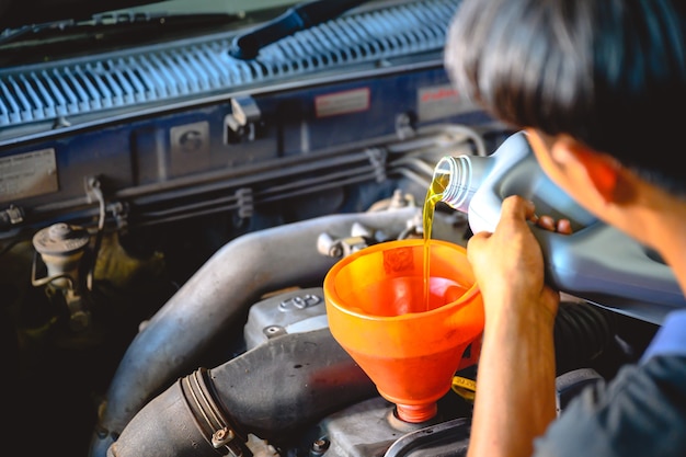 Azjatycki mechanik samochodowy pracujący w warsztacie samochodowym Wlać olej do wymiany oleju w garażu dla klientów, którzy naprawiają samochody i wymieniają olej.
