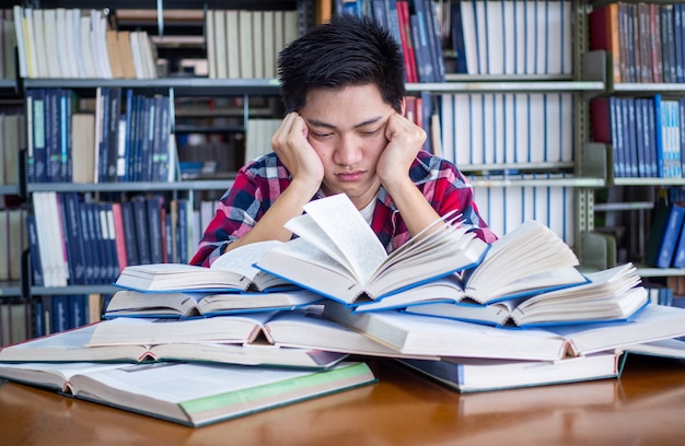 Azjatycki męski uczeń jest zmęczony i zestresowany w bibliotece