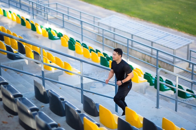 Azjatycki mężczyzna biegacz biegający wokół nowoczesnego stadionu miejskiego po schodach Cardio poranek jog wspinanie się po schodach mężczyzna jogging Outdoor sport mężczyzna sportowiec trening w krokach w mieście Aktywny fitness zdrowy styl życia