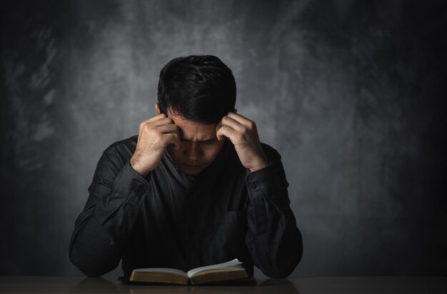 Azjatycki mężczyzna czytający książkę lub biblię przekazuje nad głową mający stresującą depresję smutny czas siedzący na stole Depresyjny mężczyzna smutny serios czytanie książki Edukacja nauka koncepcji religii biblijnej