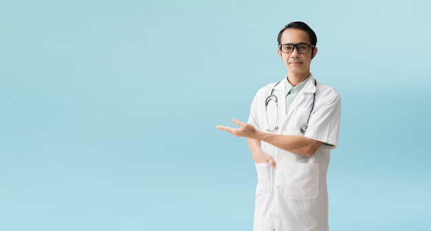 Azjatycki mężczyzna lekarz medyczny trzymający coś w pustej dłoni na białym tle na niebieskim tle ze ścieżkami przycinającymi do prac projektowych puste wolne miejsce